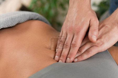 Primer plano de las manos del hombre masajista durante el masaje de estómago para su cliente mujer 