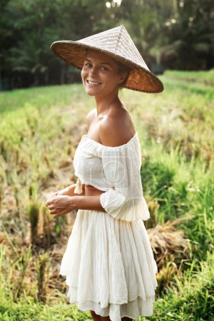 Foto de Feliz mujer sonriente con ropa natural y sombrero cónico asiático en el campo de arroz durante la puesta del sol - Imagen libre de derechos