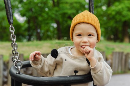 Téléchargez les photos : Portrait de mignon bébé garçon assis sur une balançoire dans le parc public - en image libre de droit