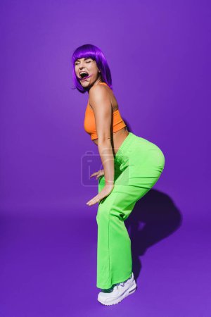 Téléchargez les photos : Femme insouciante danseuse portant des vêtements de sport colorés twerking sur fond violet - en image libre de droit