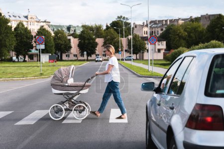 Foto de Madre joven con el cochecito de bebé está caminando por el paso de peatones. Conceptos de seguridad y código de tráfico. - Imagen libre de derechos