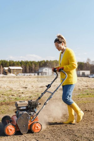 Téléchargez les photos : Jeune femme villageoise utilise une machine d'aération pour scarifier et aérer la pelouse ou le pré - en image libre de droit