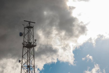 Téléchargez les photos : Vue vers le haut du sommet d'une tour de télécommunication métallique sur un fond de ciel avec un grand nuage blanc. - en image libre de droit