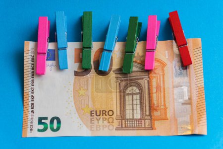 Foto de Primer plano de pinzas de madera coloridas unidas a un billete de cincuenta euros sobre fondo azul. - Imagen libre de derechos