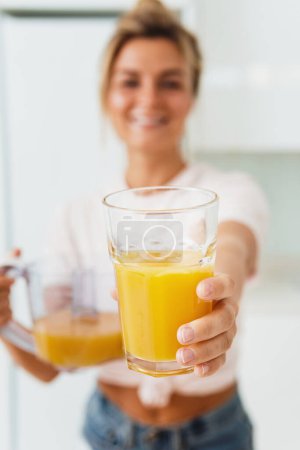 Foto de Joven mujer alegre con gran vaso de jugo de naranja fresco en casa. Concéntrate en el vidrio. - Imagen libre de derechos