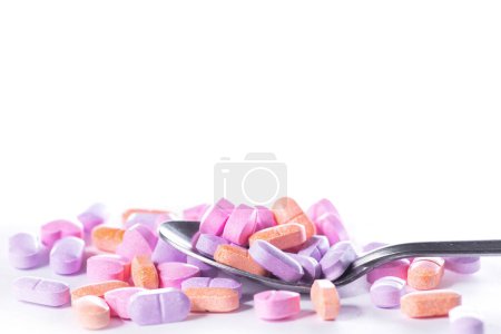 Foto de Primer plano de una cuchara metálica y una pila de píldoras de colores sobre fondo blanco. - Imagen libre de derechos