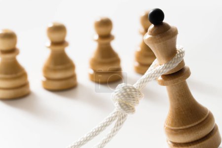 Photo for Closeup shot of a white rope pulling down a wooden chess queen with several chessmen nearby. Concept of facing public disapproval and being burdened by responsibility. - Royalty Free Image