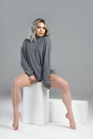 Téléchargez les photos : Portrait de jeune femme sexy aux cheveux blonds portant un pull à col roulé pose sur fond gris en studio - en image libre de droit