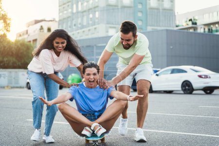 Photo for Three diverse carefree friends having fun and riding longboard on parking lot - Royalty Free Image