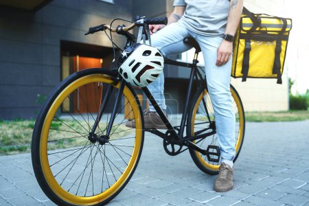 Téléchargez les photos : Messager de livraison express avec sac isolé sur le dos est assis sur son vélo avec casque de vélo accroché sur son volant. - en image libre de droit