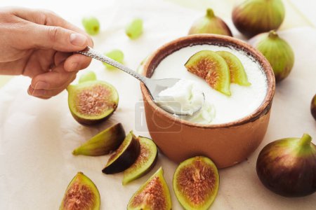 Photo for Closeup of spoon and delicious natural Greek yogurt in clay bowl with figs - Royalty Free Image