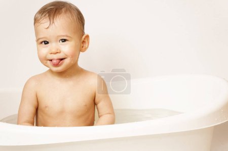 Foto de Adorable niño sonriente está pegando una lengua mientras toma un baño en agua tibia. - Imagen libre de derechos