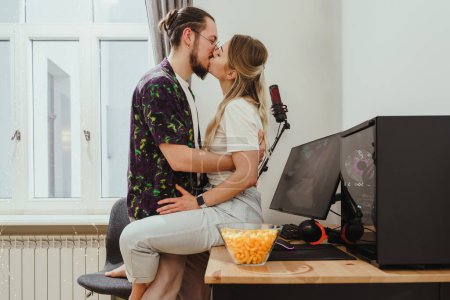 Foto de Joven y sensual pareja besándose en la mesa con el juego de ordenador personal - Imagen libre de derechos