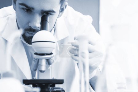 Photo for Man scientist is using microscope in a laboratory during science research work. Tinted in blue monochrome colors for scientific look. - Royalty Free Image