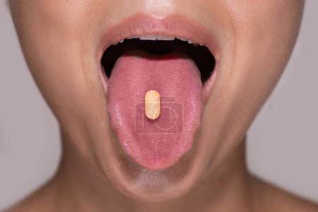 Foto de Primer plano de una parte inferior de una cara femenina joven con una pastilla naranja en la lengua. - Imagen libre de derechos