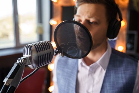 Téléchargez les photos : Jeune homme barbu beau chante dans un microphone dans un studio de musique maison - en image libre de droit