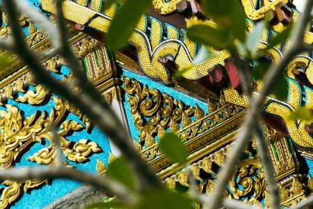 Photo for Closeup shot of beautiful bright architecture decorations in ancient buddhist temple in Thailand with tree branches in foreground. - Royalty Free Image