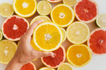Photo for Closeup of female hand with half of orange against citrus fruits background - Royalty Free Image