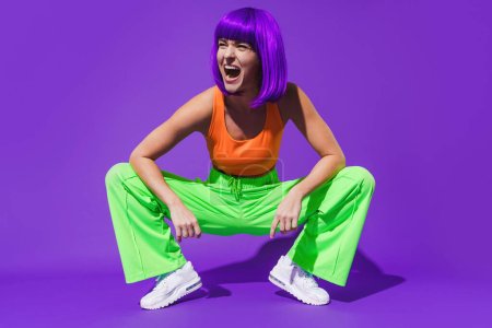 Téléchargez les photos : Portrait de femme joyeuse portant des vêtements de sport colorés sur fond violet - en image libre de droit