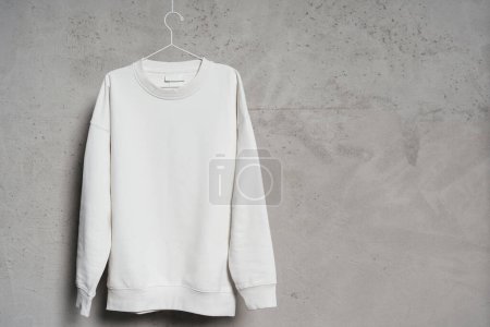 Photo for Mockup of blank white sweatshirt hanging on the thin metallic hanger against a concrete wall - Royalty Free Image