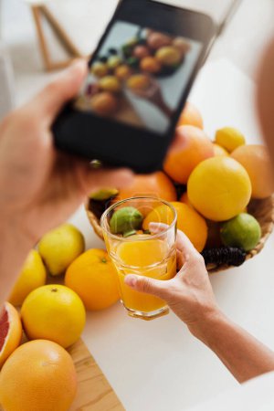 Photo for Closeup of female hand with a smartphone taking photos of glass with orange juice - Royalty Free Image
