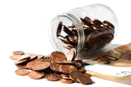Foto de Primer plano de un billete de cincuenta euros y monedas de cobre brillante de bajo valor derramadas de un frasco de vidrio. - Imagen libre de derechos