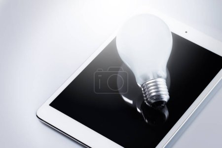 Photo for Closeup of light bulb lying on white tablet computer. Concept of innovation and solutions in business. - Royalty Free Image