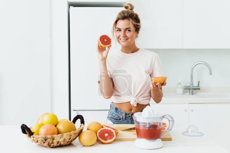 Photo for Young cheerful woman with ripe grapefruits making fresh juice at home - Royalty Free Image