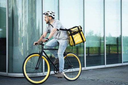 Téléchargez les photos : Jeune messager express livraison de nourriture est sur un vélo avec un sac isolé derrière son dos. - en image libre de droit