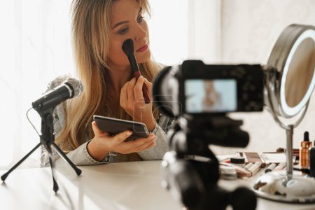 Young woman beauty blogger applying blush powder on her face during video recording for her followers