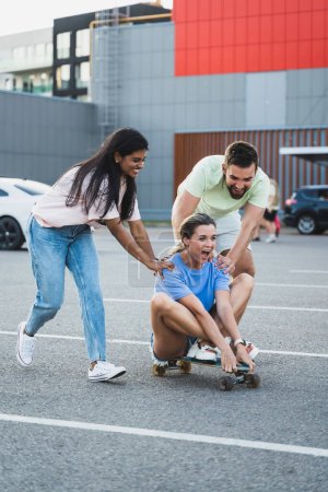 Photo for Three diverse carefree friends having fun and riding longboard on parking lot - Royalty Free Image