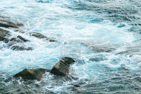 Téléchargez les photos : Gros plan de vagues mousseuses s'écrasant sur une côte rocheuse à marée haute. - en image libre de droit