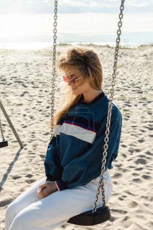 Photo for Young pretty woman is sitting on the swing and smiling at the sandy beach. - Royalty Free Image