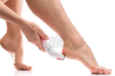 Foto de Primer plano de pies femeninos y archivo de pie eléctrico para el callo y la eliminación de la piel muerta sobre fondo blanco - Imagen libre de derechos