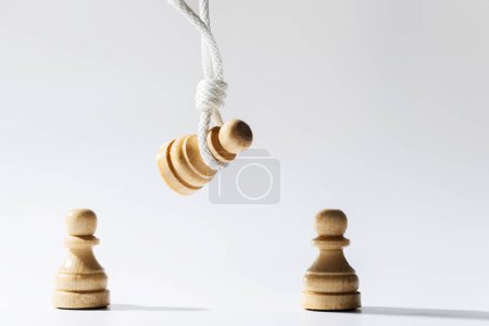Foto de Primer plano de un peón de ajedrez de madera colgado en una cuerda blanca con otros peones de pie debajo. Concepto de discriminación y desaprobación pública. - Imagen libre de derechos
