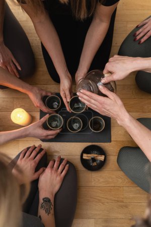 Photo for Young woman is pouring hot tea to her friends sitting around a tray during a tea ceremony. - Royalty Free Image