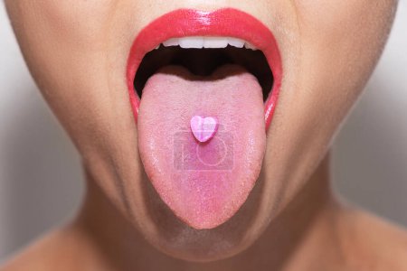 Foto de Primer plano de una parte inferior de una cara femenina joven con una píldora rosa en forma de corazón en su lengua - Imagen libre de derechos