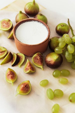 Téléchargez les photos : Délicieux yaourt grec naturel dans un bol en argile avec des figues et du raisin sur papier parchemin blanc - en image libre de droit