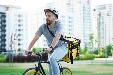 Foto de Joven mensajero de reparto de comida express está montando una bicicleta con una bolsa aislada detrás de su espalda. - Imagen libre de derechos
