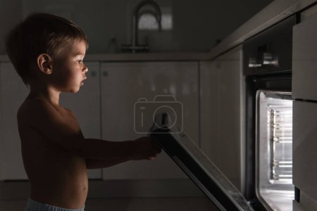 Foto de Lindo bebé curioso abre el horno caliente. Concepto de seguridad y posibles problemas con niños desatendidos. - Imagen libre de derechos