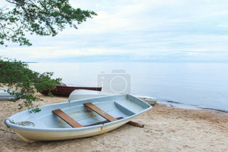 Photo for Closeup shot of a abandoned shabby fishing boats lying on a sandy beach near the calm sea water. - Royalty Free Image
