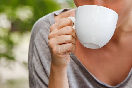 Foto de Primer plano de una joven mujer bonita sentada en un café al aire libre y tomando café de una taza de cerámica blanca. - Imagen libre de derechos