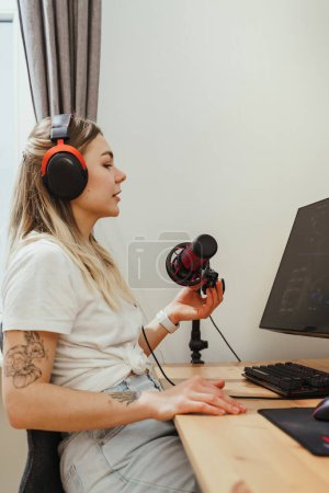 Photo for Young  woman blogger using headphones and condenser microphone during online podcast at home - Royalty Free Image