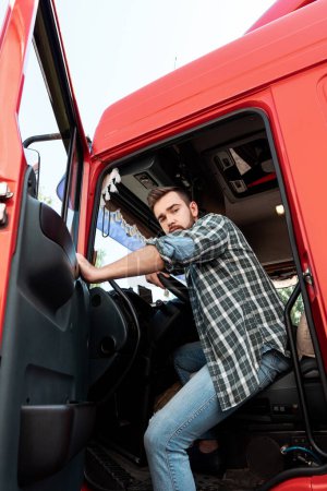Téléchargez les photos : Beau chauffeur de camion barbu assis à l'intérieur de son camion de fret rouge - en image libre de droit