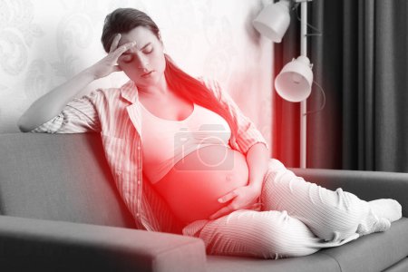 Photo for Young pregnant woman lying on the sofa at home with a painful headache - Royalty Free Image