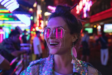 Photo for Young stylish woman wearing jacket with shining sequins on the city street with neon lights - Royalty Free Image
