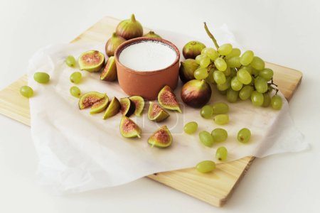 Téléchargez les photos : Délicieux yaourt grec naturel dans un bol en argile avec des figues et du raisin sur papier parchemin blanc - en image libre de droit