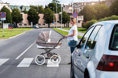 Téléchargez les photos : La jeune mère avec le landau marche sur le passage pour piétons. Concepts de sécurité et code de la route. - en image libre de droit