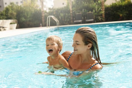 Foto de Feliz madre y su lindo hijo nadando en la piscina al aire libre durante las vacaciones de verano - Imagen libre de derechos