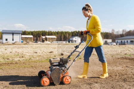 Téléchargez les photos : Jeune femme villageoise utilise une machine d'aération pour scarifier et aérer la pelouse ou le pré - en image libre de droit